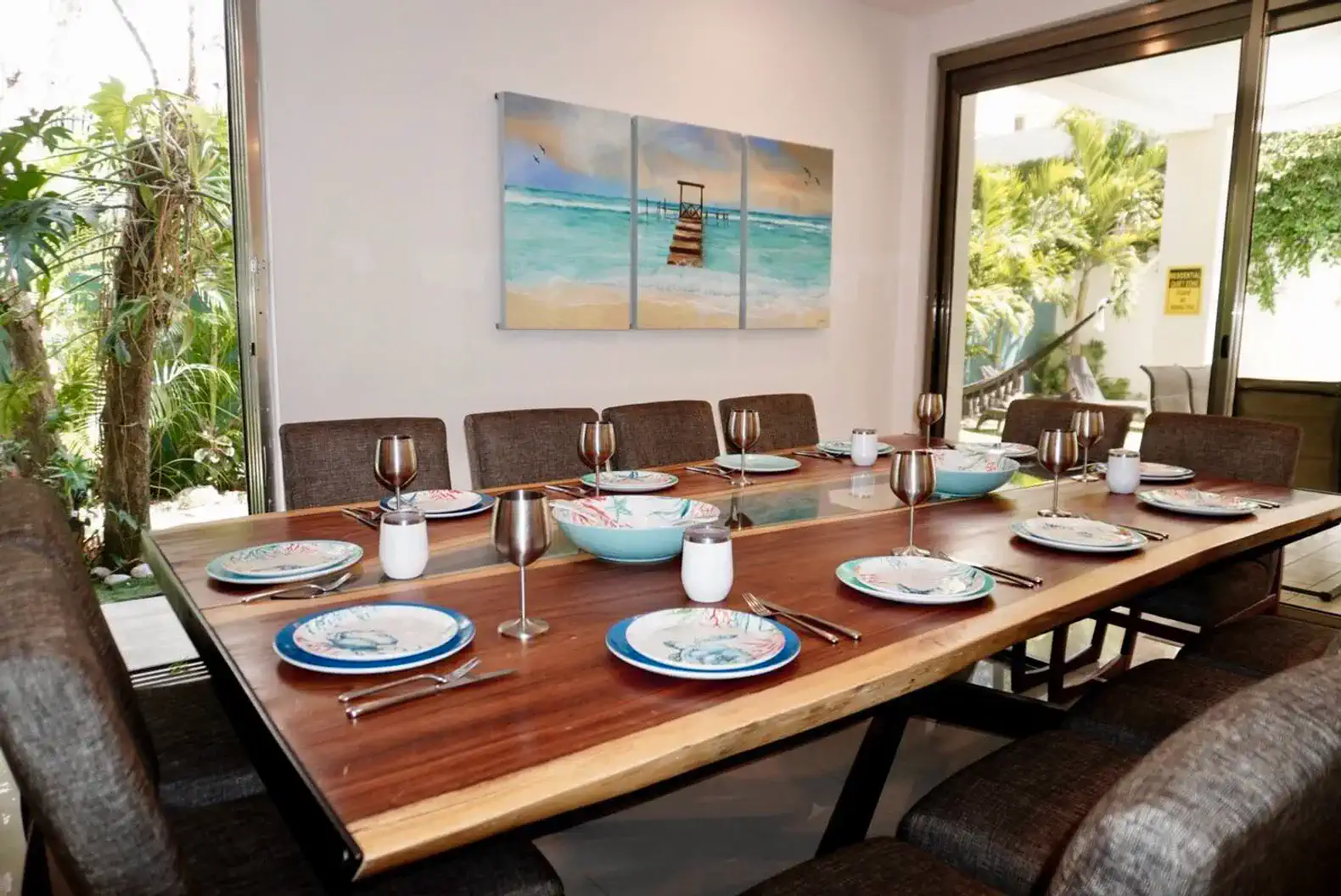 Mesa de comedor elegante con platos y copas, rodeada de vegetación tropical