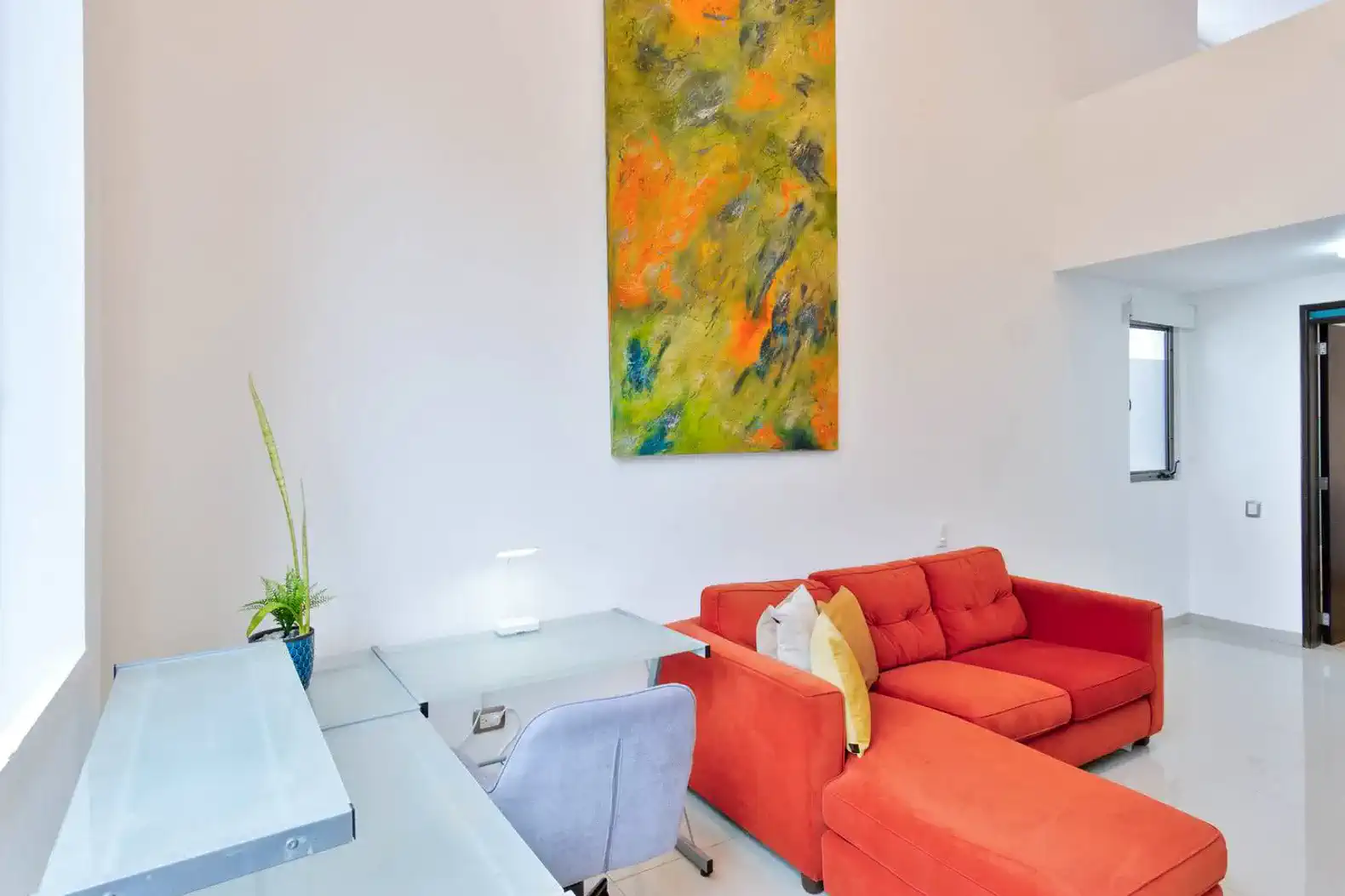 Sala de estar moderna con sofá rojo y escritorio, decorada con arte contemporáneo