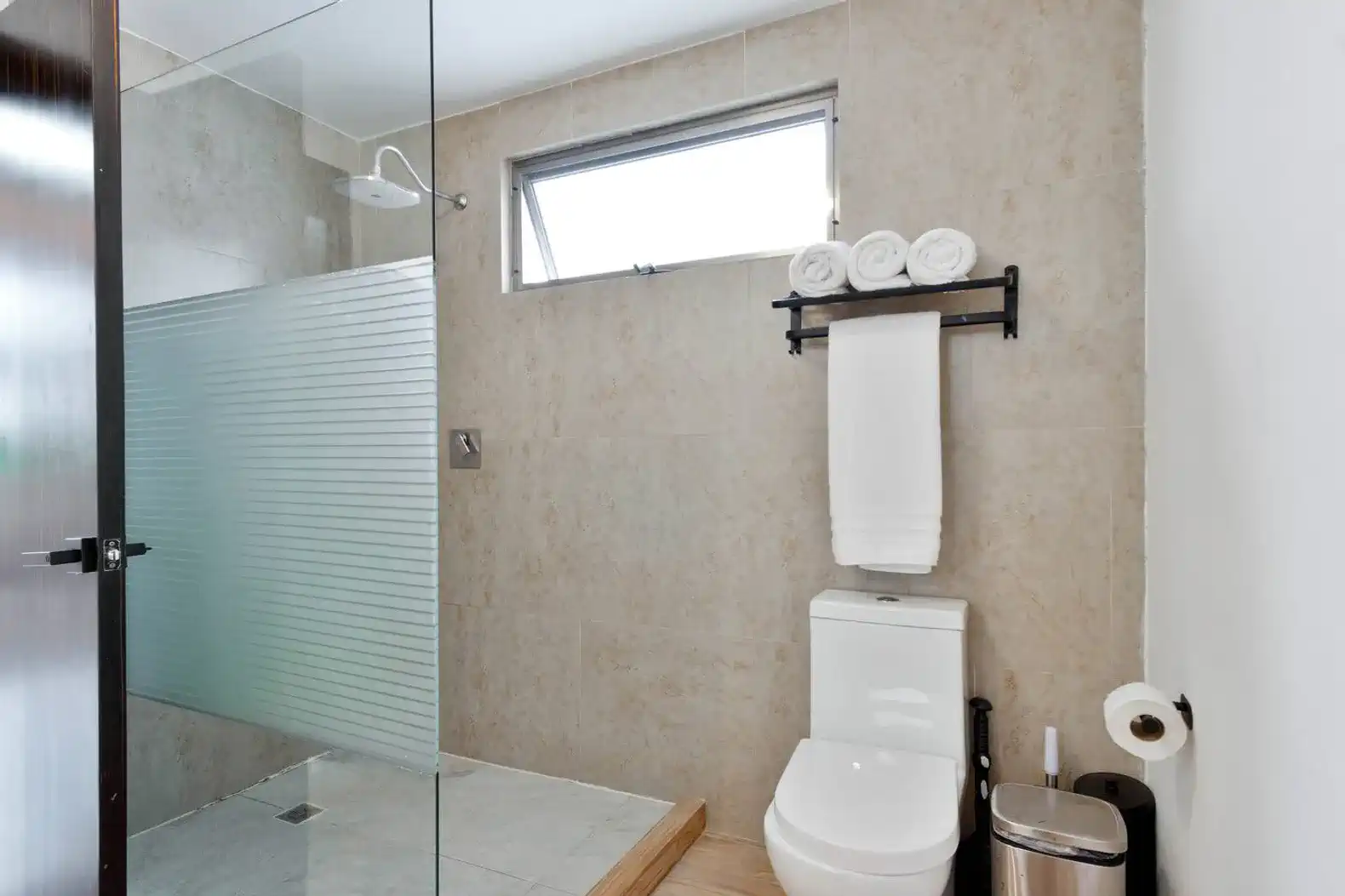 Baño moderno con ducha de vidrio y toallas blancas enrolladas