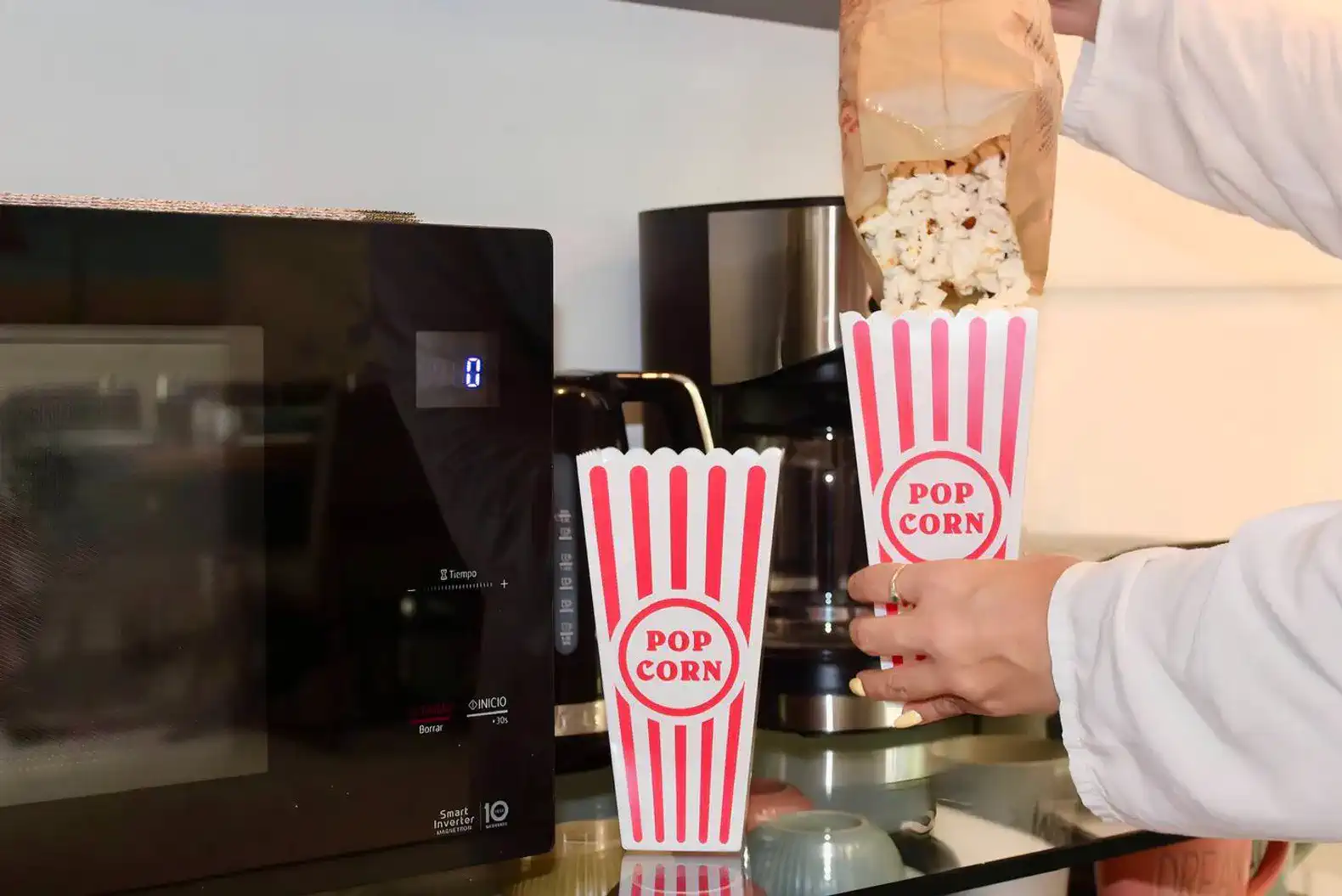 Dos recipientes de palomitas de maíz siendo llenados desde una bolsa en una cocina moderna