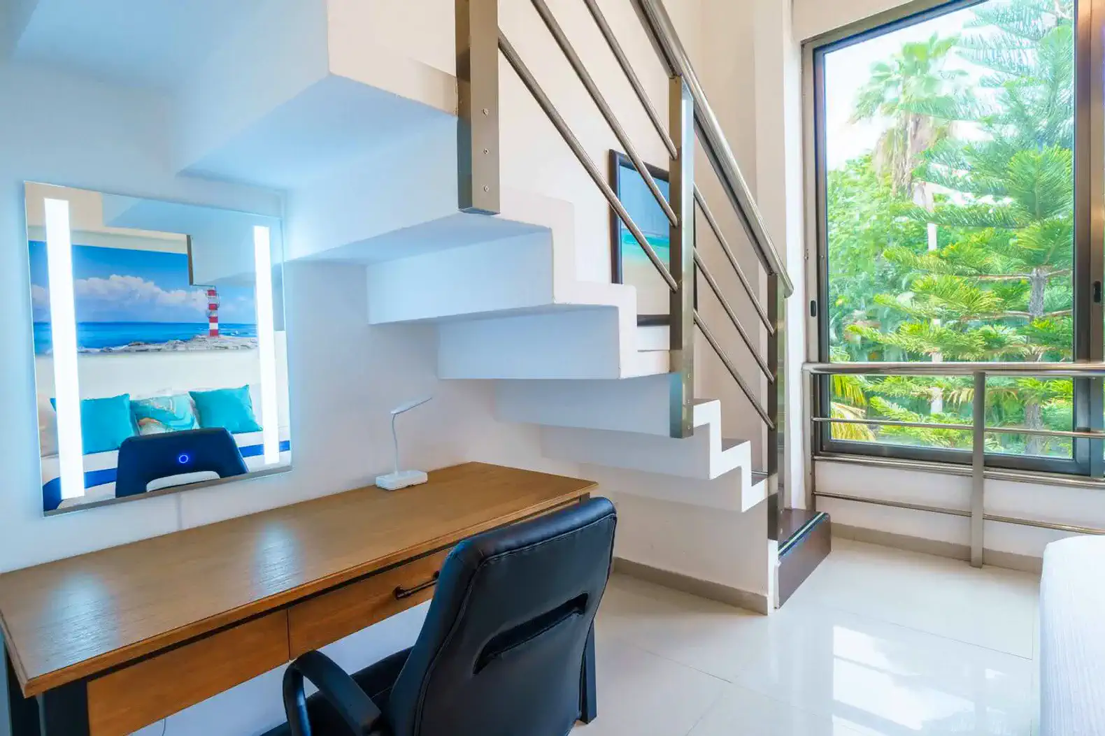 Escritorio moderno junto a una ventana con vista a la vegetación y escaleras en un ambiente luminoso