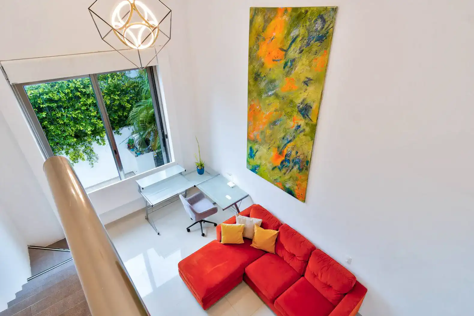 Sala de estar con sofá rojo, escritorio y ventana grande con vista a la vegetación