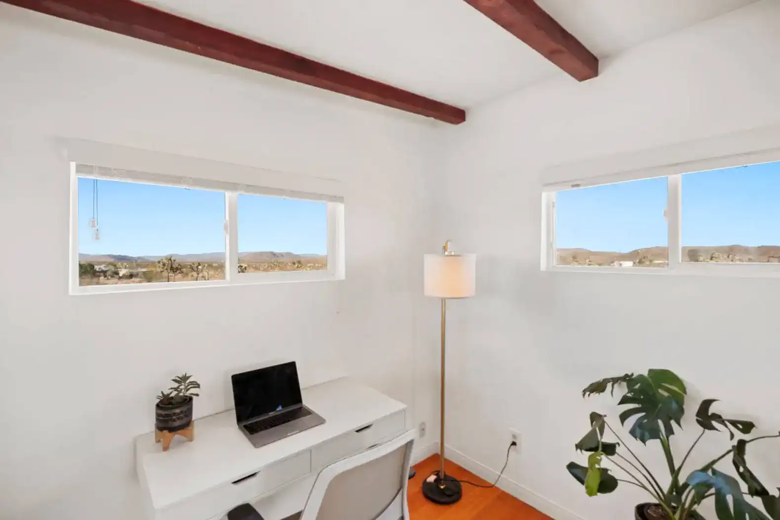 Bright workspace with a desk, laptop, and windows showcasing desert views
