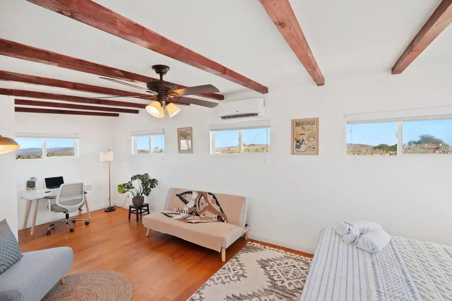 Bright and airy master bedroom with wooden beams, a sofa, and a workspace