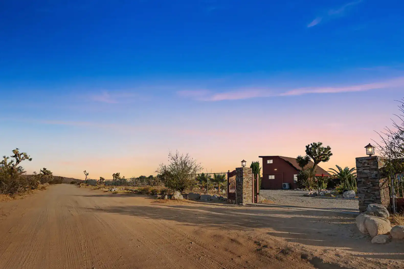 Rustic entrance with stone pillars leading to a charming cabin surrounded by desert landscape