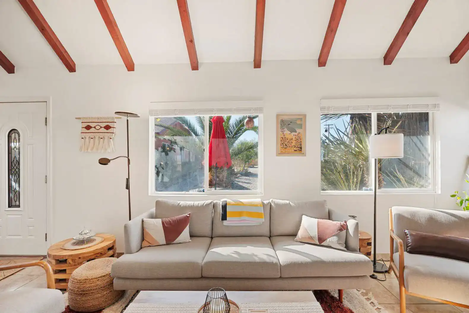 Cozy living room with a modern sofa, wooden beams, and large windows overlooking greenery
