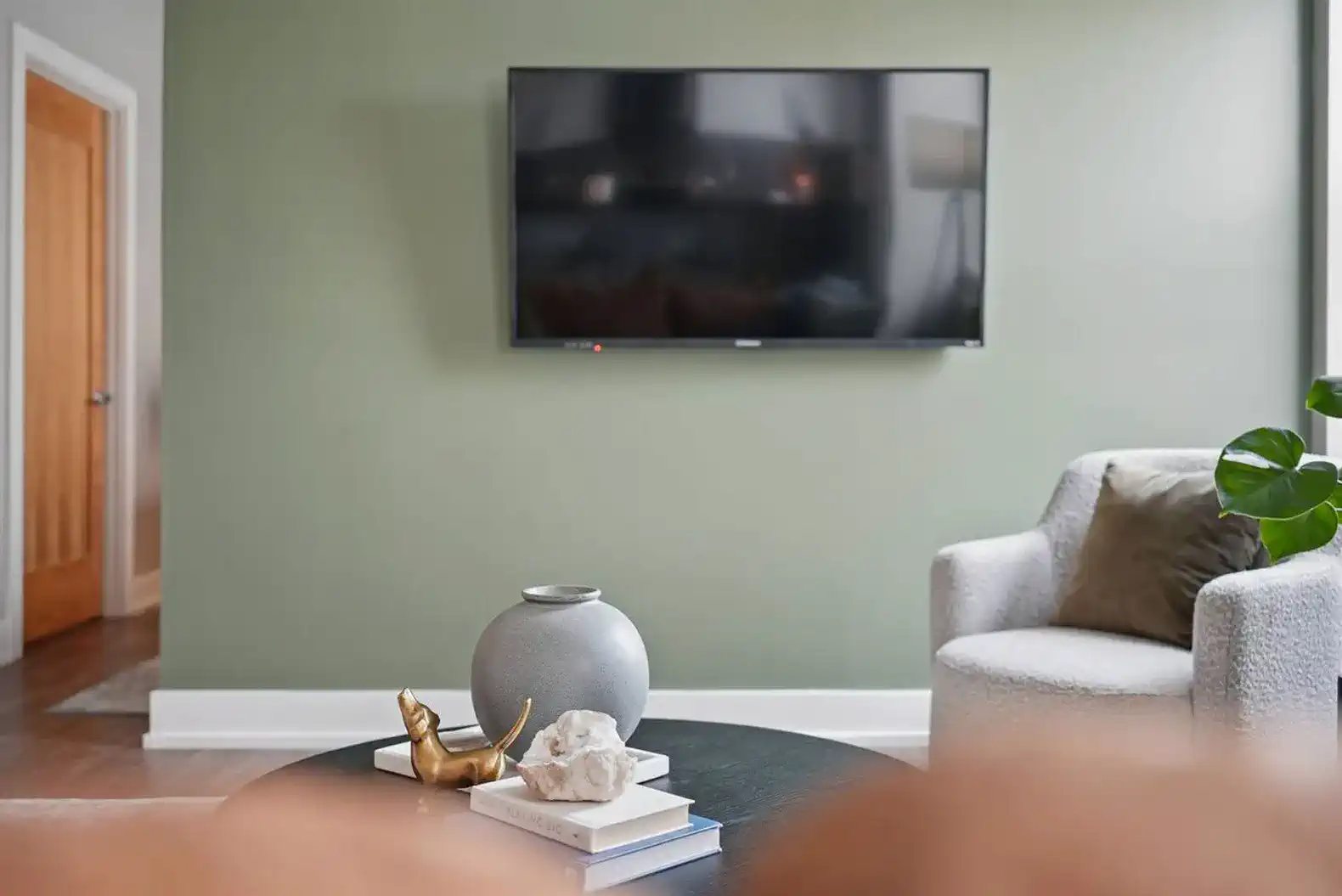 Relax in a stylish living room with a mounted flatscreen TV, curated decor, and a calming green accent wall.