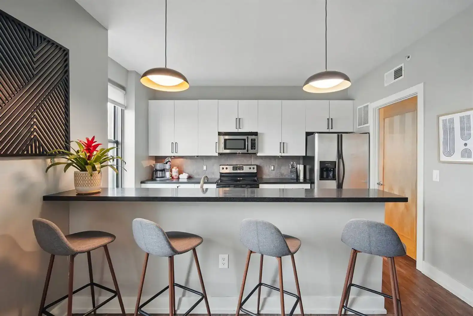 Stylish kitchen with sleek black countertops, modern pendant lighting, and seating for four—perfect for morning coffee or late-night snacks.
