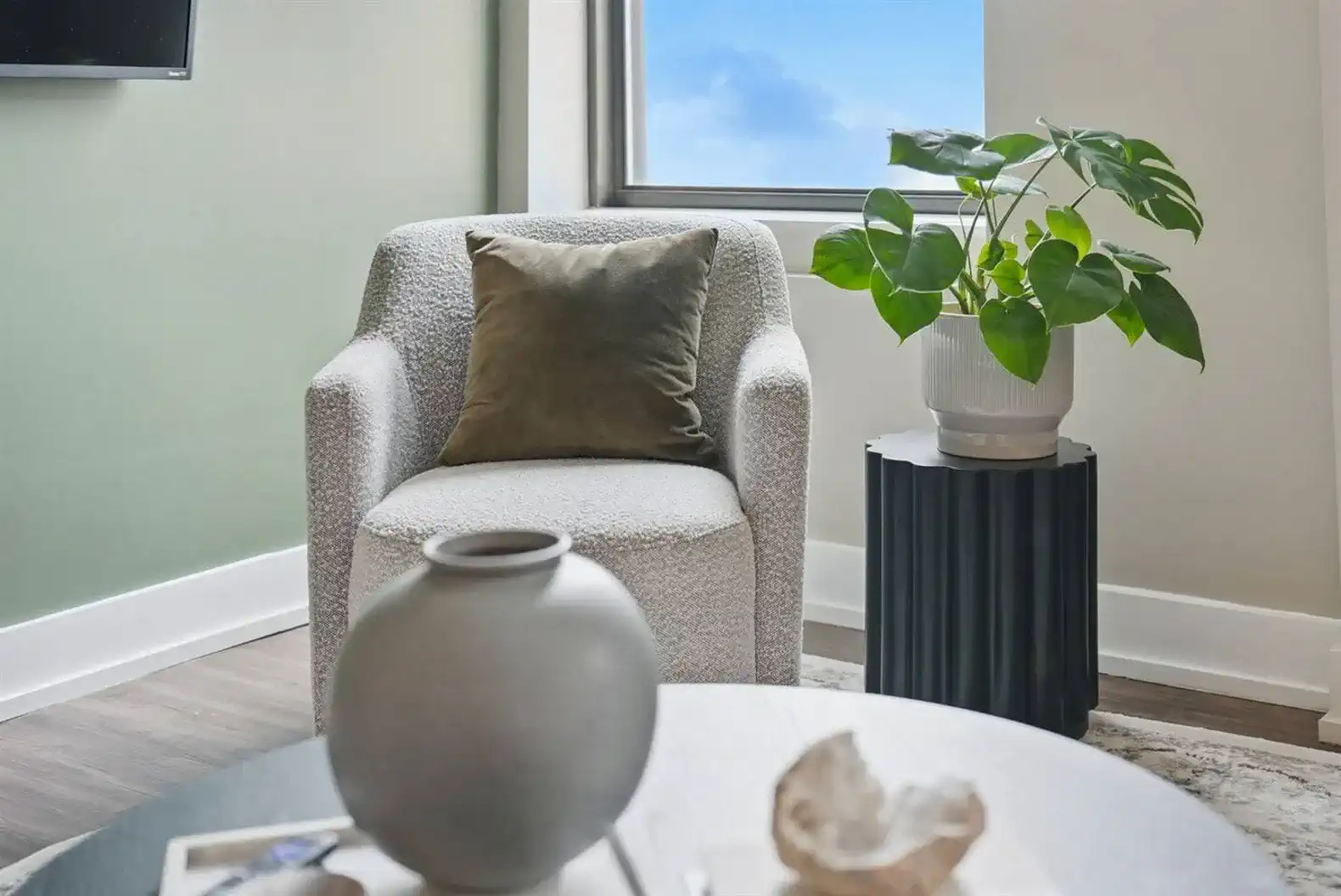 Cozy up in a modern reading chair with a plush pillow and natural light, next to a chic black side table and leafy green plant.