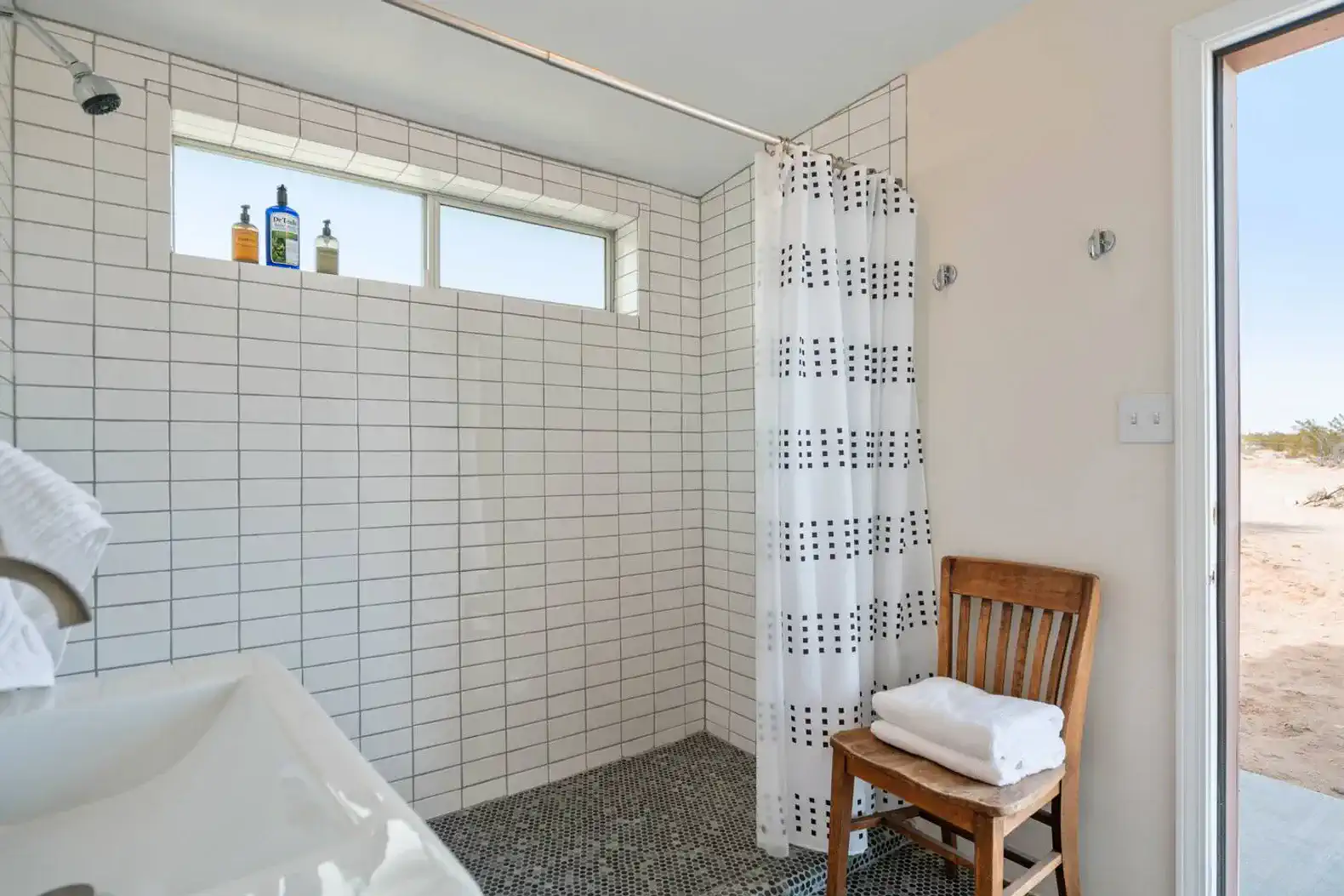 Modern bathroom with tiled shower, window for natural light, and wooden chair