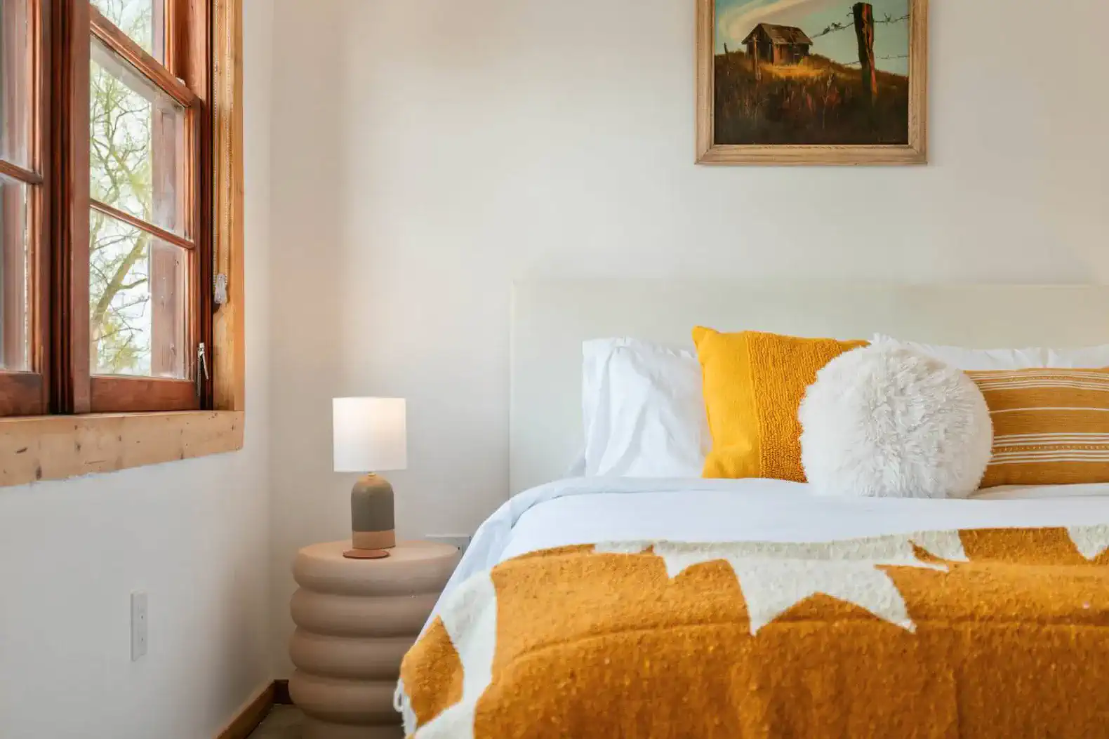 Cozy guest bedroom with warm tones, a plush blanket, and natural light from large windows