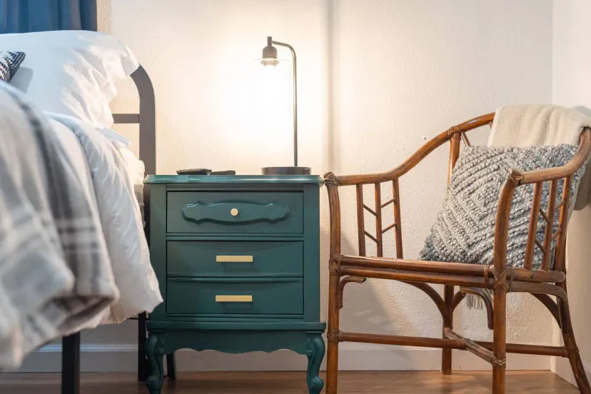 Acogedora mesa de noche con lámpara y una silla de ratán en un ambiente de dormitorio