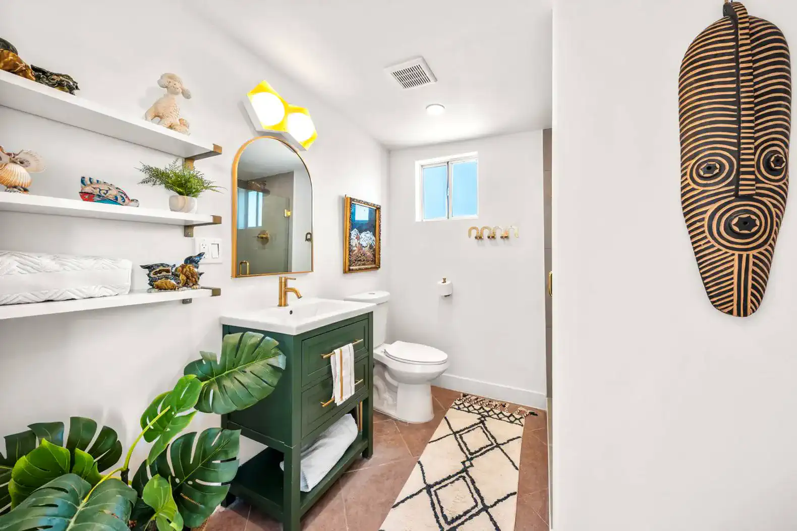 Bright bathroom featuring a green vanity, decorative shelves, and tropical plants