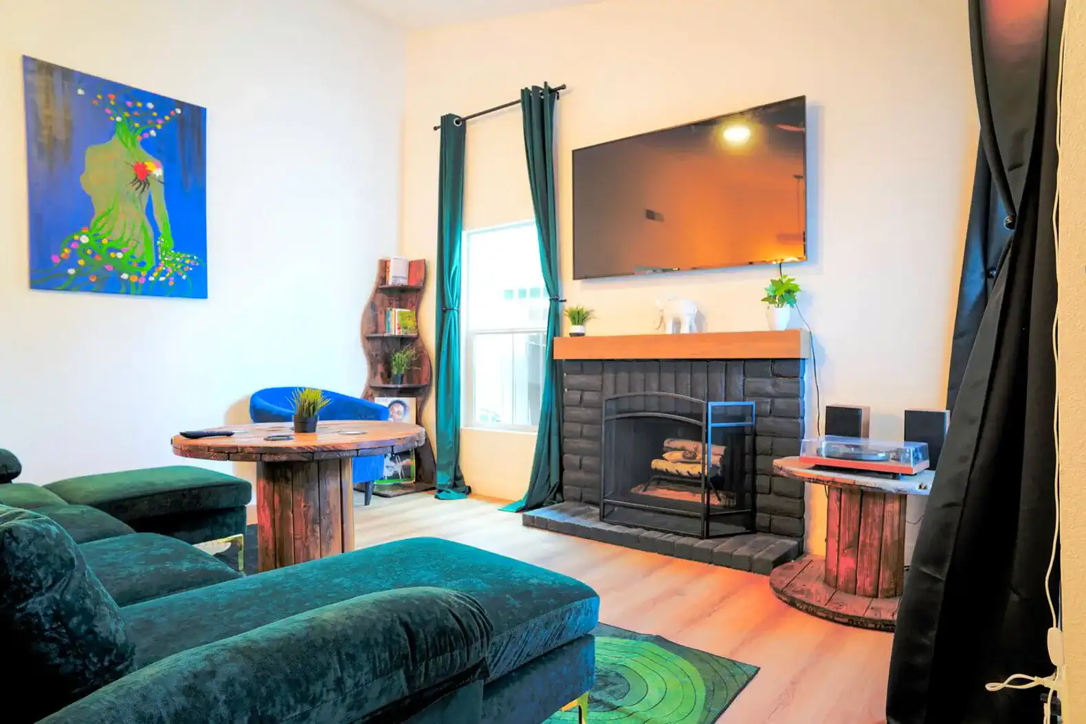 Cozy living room with a fireplace, green velvet seating, and colorful artwork