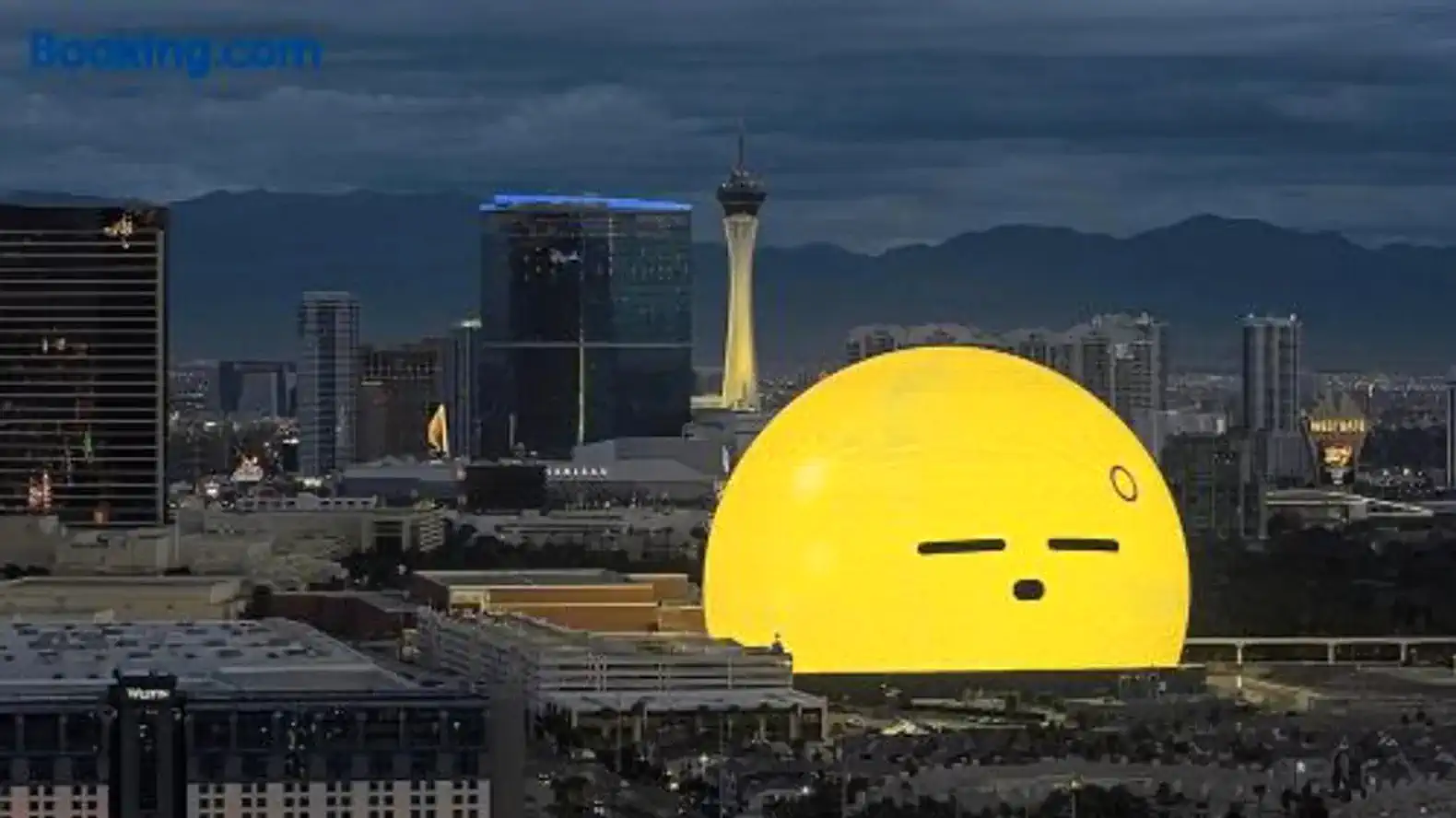 View of a large yellow structure resembling a smiling sun against a city skyline