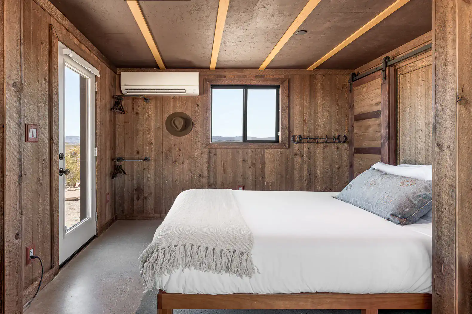 Cozy master bedroom with wooden walls and a queen bed, featuring a window and air conditioning