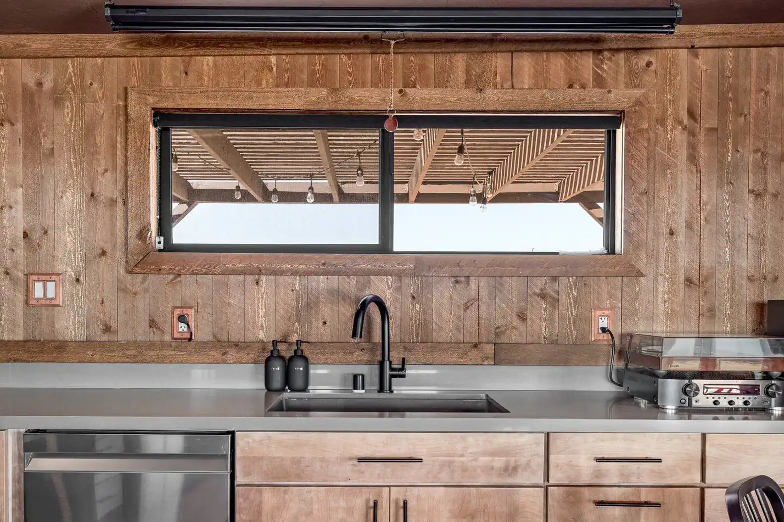 Modern kitchen with wooden walls, sleek sink, and large window overlooking outdoor area