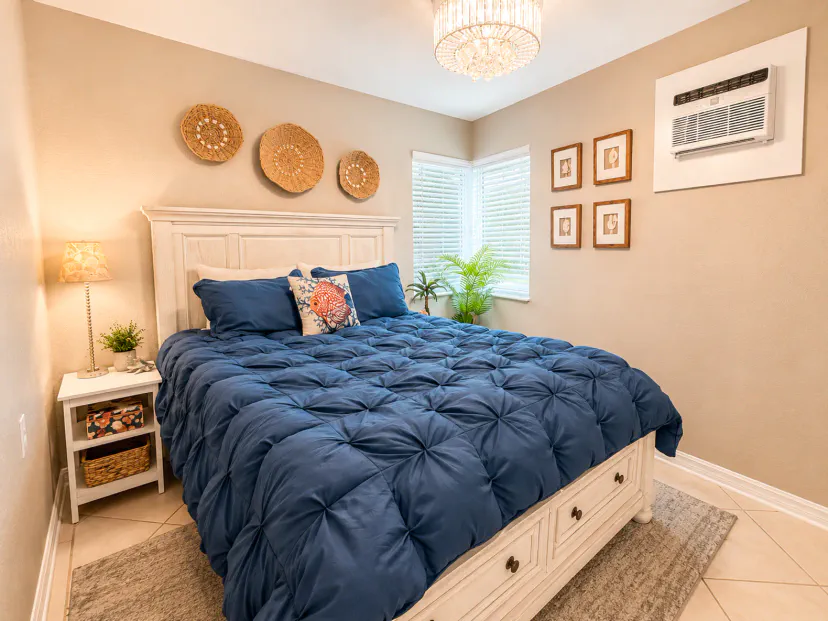 Cozy, sunlit bedroom with plush bedding, chandelier, and in-room AC