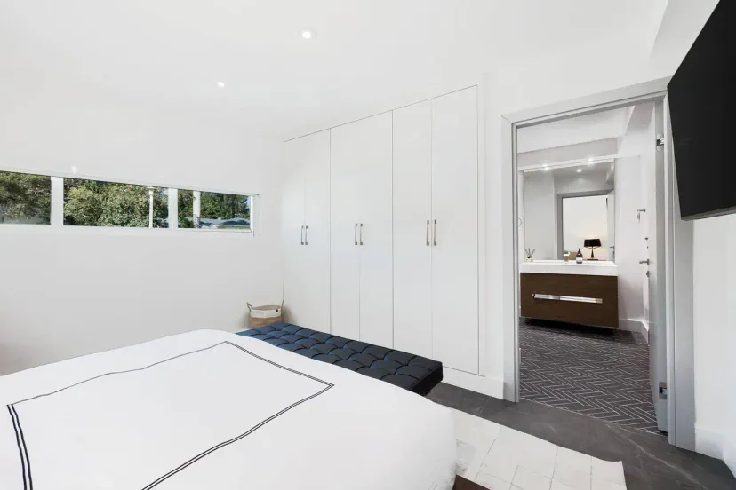 Cama king size del dormitorio anterior con un televisor inteligente y un baño compartido que conecta con la otra habitación.
