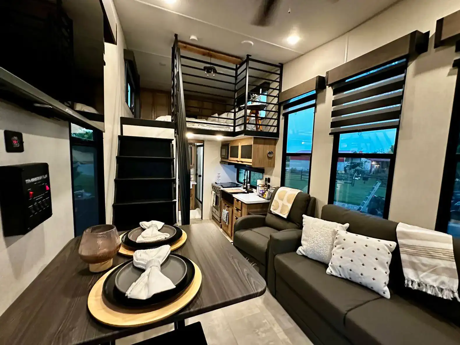 Cozy living area with modern decor, staircase leading to loft, and kitchen in the background