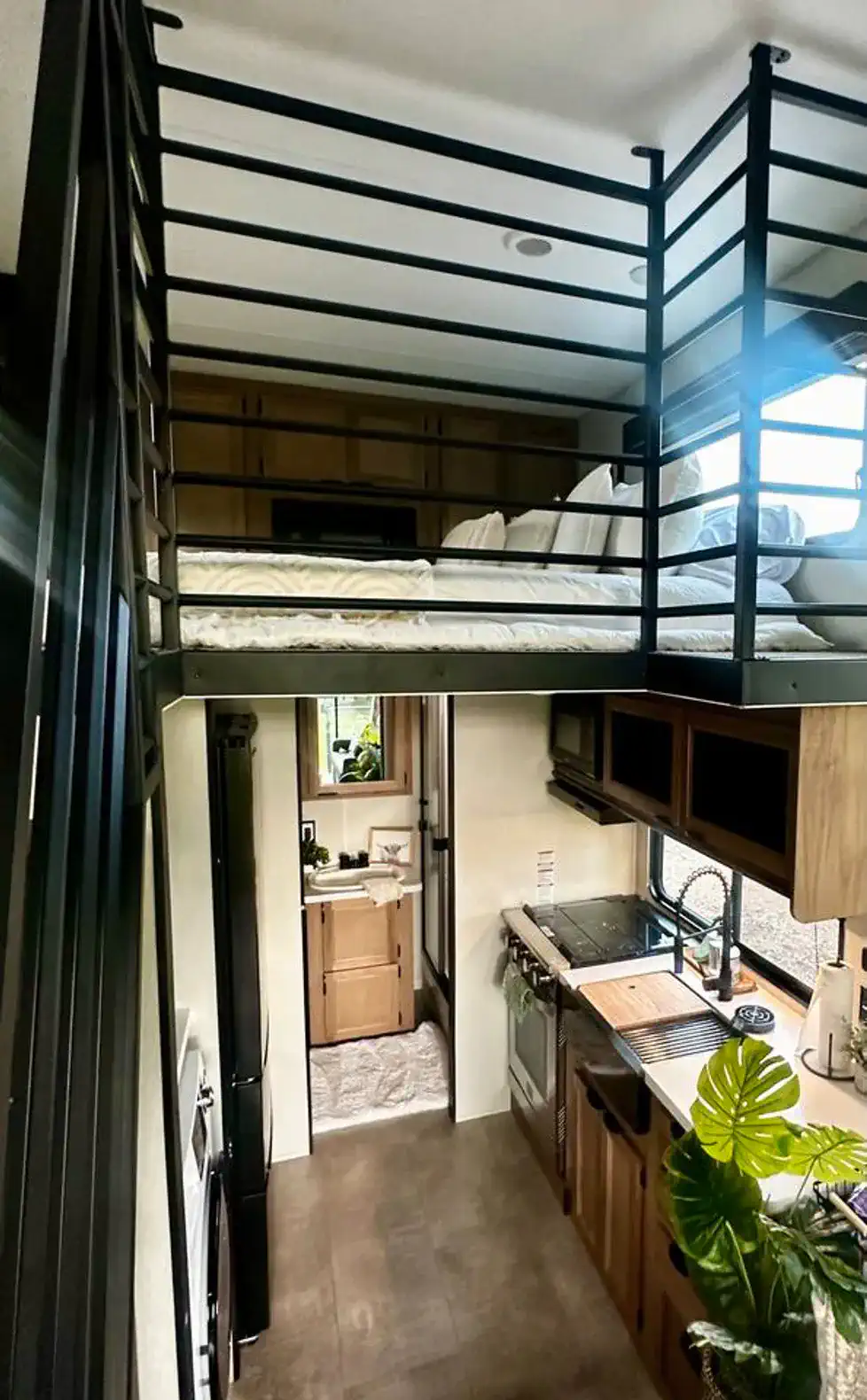 Lofted bed above a modern kitchen and bathroom area in a compact space