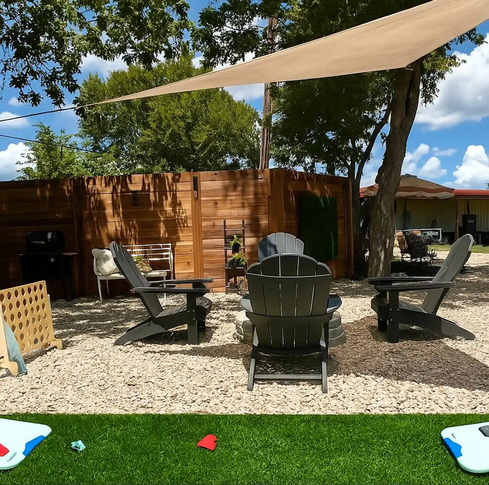 Outdoor seating area with Adirondack chairs and shade sail in a landscaped yard