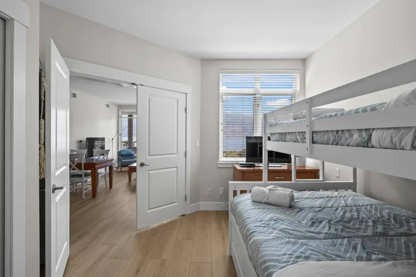 Cozy bedroom with a bunk bed and a twin bed, leading to a living area with a dining table and TV