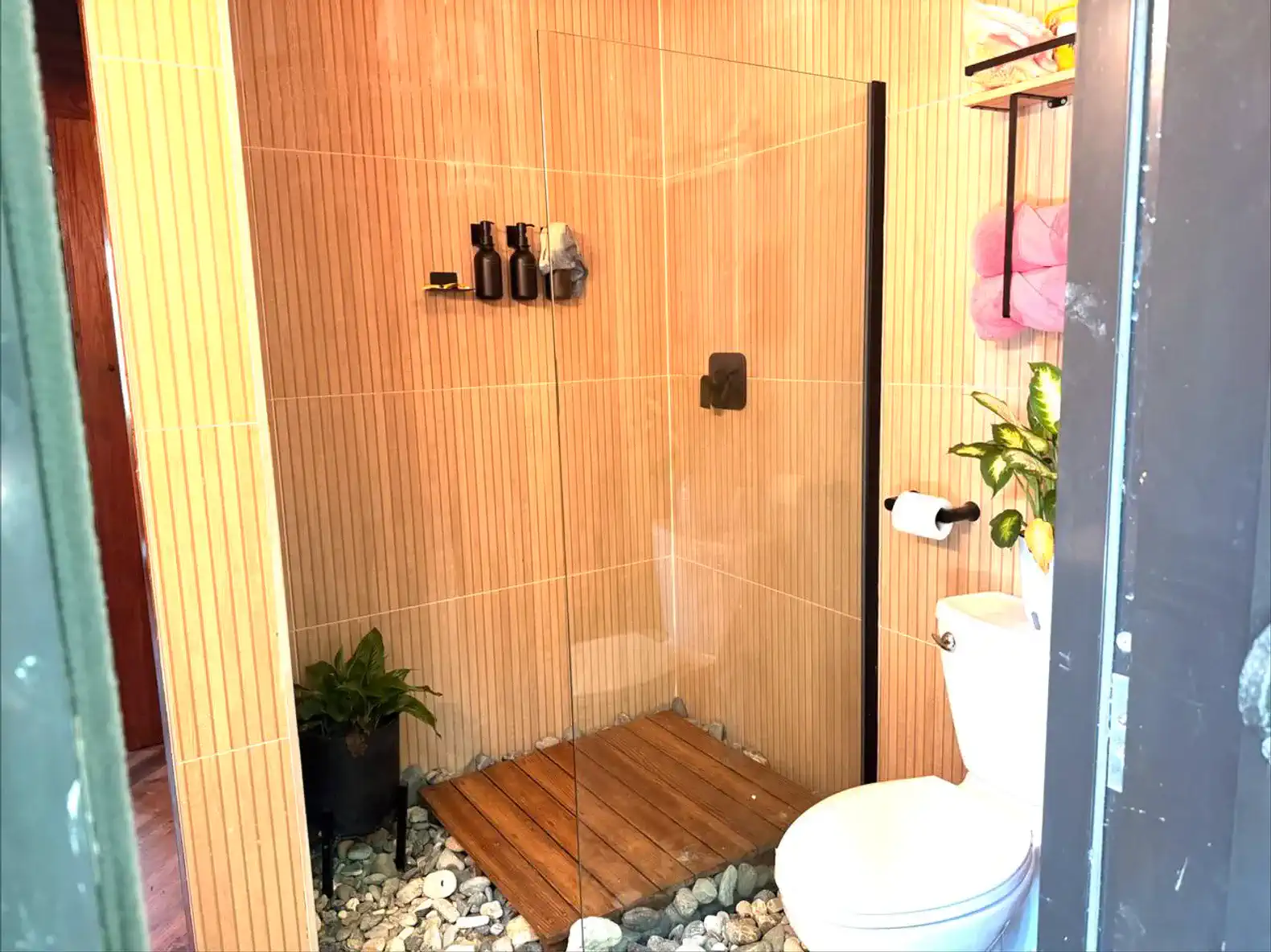 Modern shower with glass enclosure, wooden floor, and decorative plants