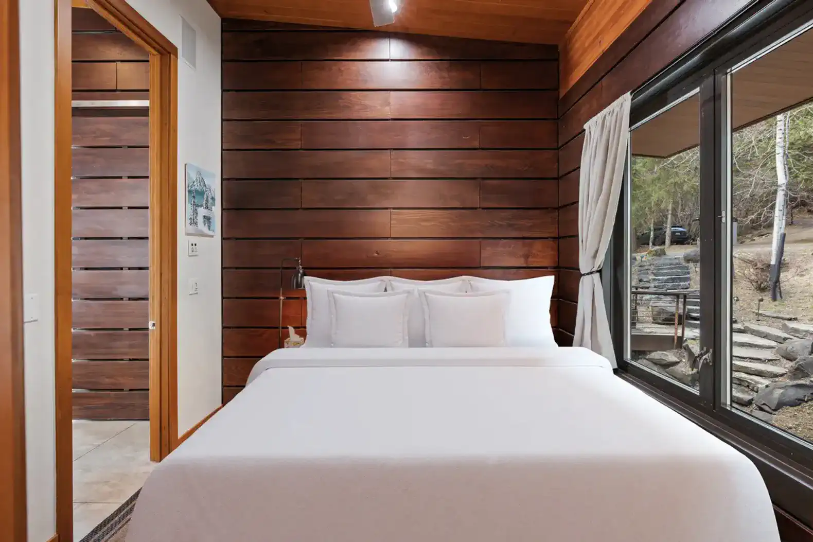 Cozy master bedroom with wooden walls and large window overlooking nature