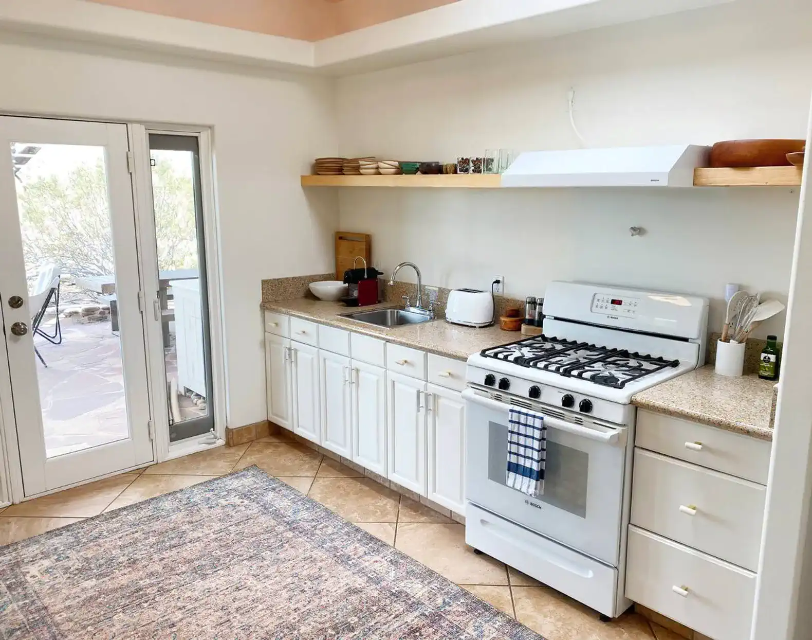 Bright kitchen with white cabinets, gas stove, and access to outdoor seating area