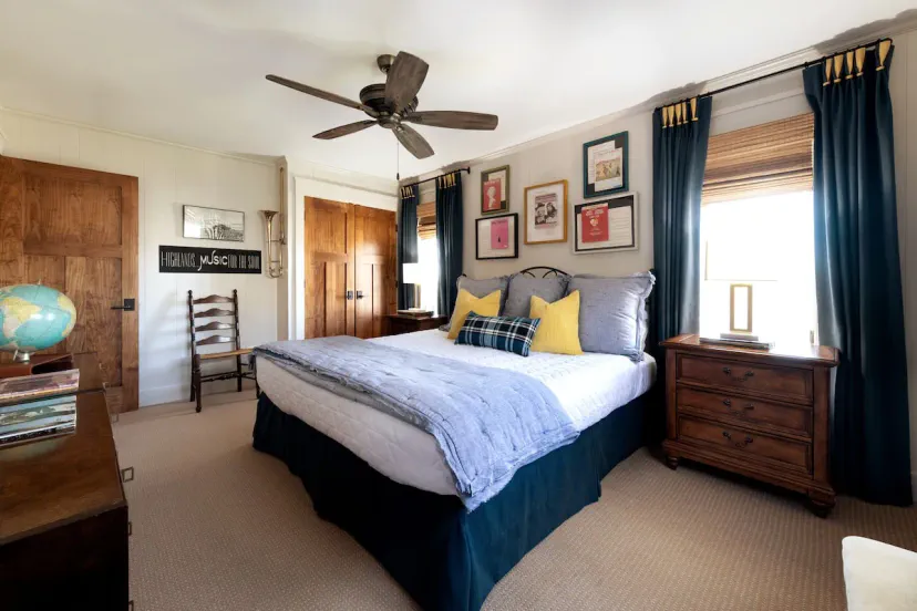 Charmantes Gästezimmer mit marineblauen Bettwäsche, gelben Akzentkissen, Galerie-Wandkunst und eklektischer Berghütten-Dekoration — das zweite Schlafzimmer im High House bietet Gästen stilvollen Schlaf nahe Highlands und Cashiers, NC.