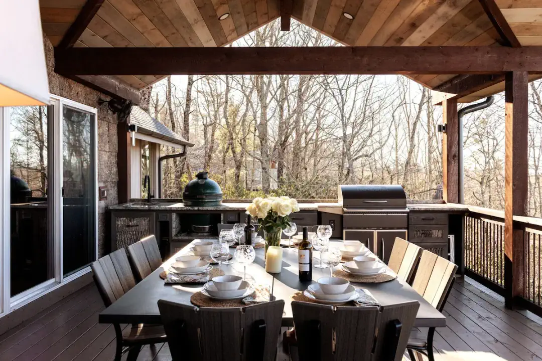 Alfresco-Essen in Perfektion — überdachte Außenterrasse mit Big Green Egg, Gasgrill und einem vollständig gedeckten Esstisch für 10 Personen, umgeben von Blick auf die Blue Ridge Mountains in Highlands, NC