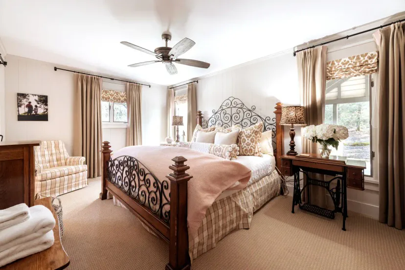 Romantisches drittes Schlafzimmer mit kunstvollem Eisenkopfteil, rosafarbenen Bettwäsche und einem antiken Nähmaschinen-Nebentisch — jedes Zimmer im High House erzählt seine eigene Geschichte nahe Highlands und Cashiers, NC.