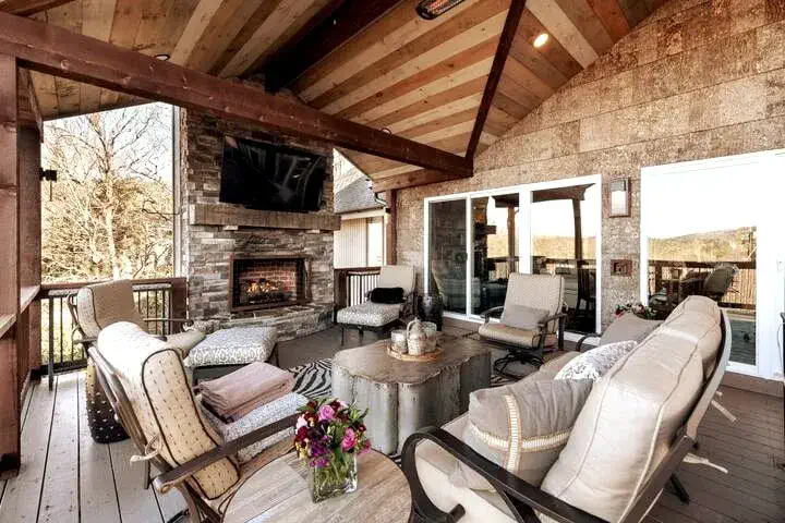 Überdachtes Wohnzimmer im Freien mit Steinkamin, Außenfernseher und bequemen Sitzgelegenheiten — genießen Sie die Blue Ridge Mountains bei jedem Wetter im High House nahe Highlands, NC, von frischen Herbstabenden bis zu sternenklaren Nächten.