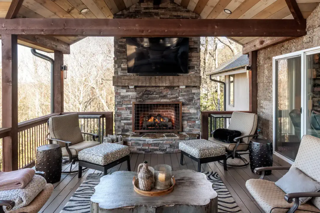 Vier Jahreszeiten im Freien in seiner besten Form — überdachte Veranda mit loderndem Steinkamin, montiertem Fernseher und bequemen Sitzgelegenheiten, perfekt für kühle Abende in den Blue Ridge Mountains in Highlands, NC