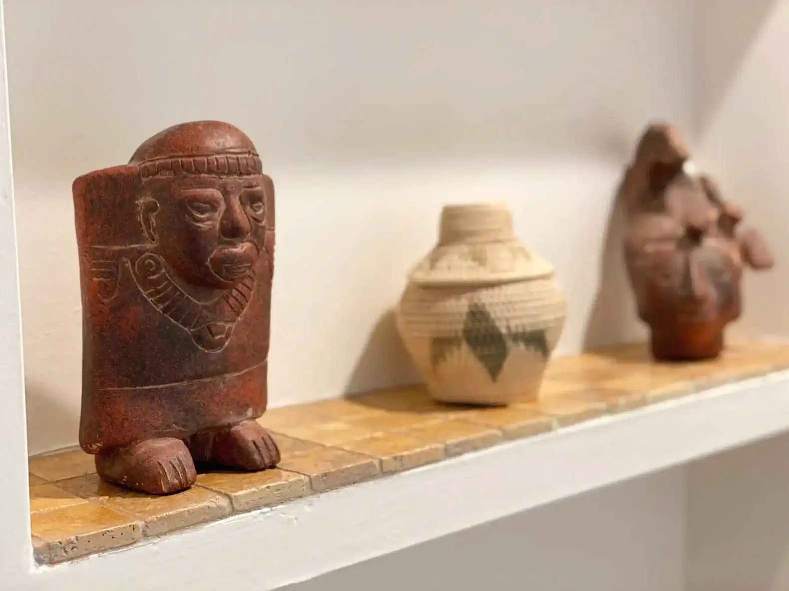 Decorative artifacts displayed on a shelf, including a carved figure and woven pottery
