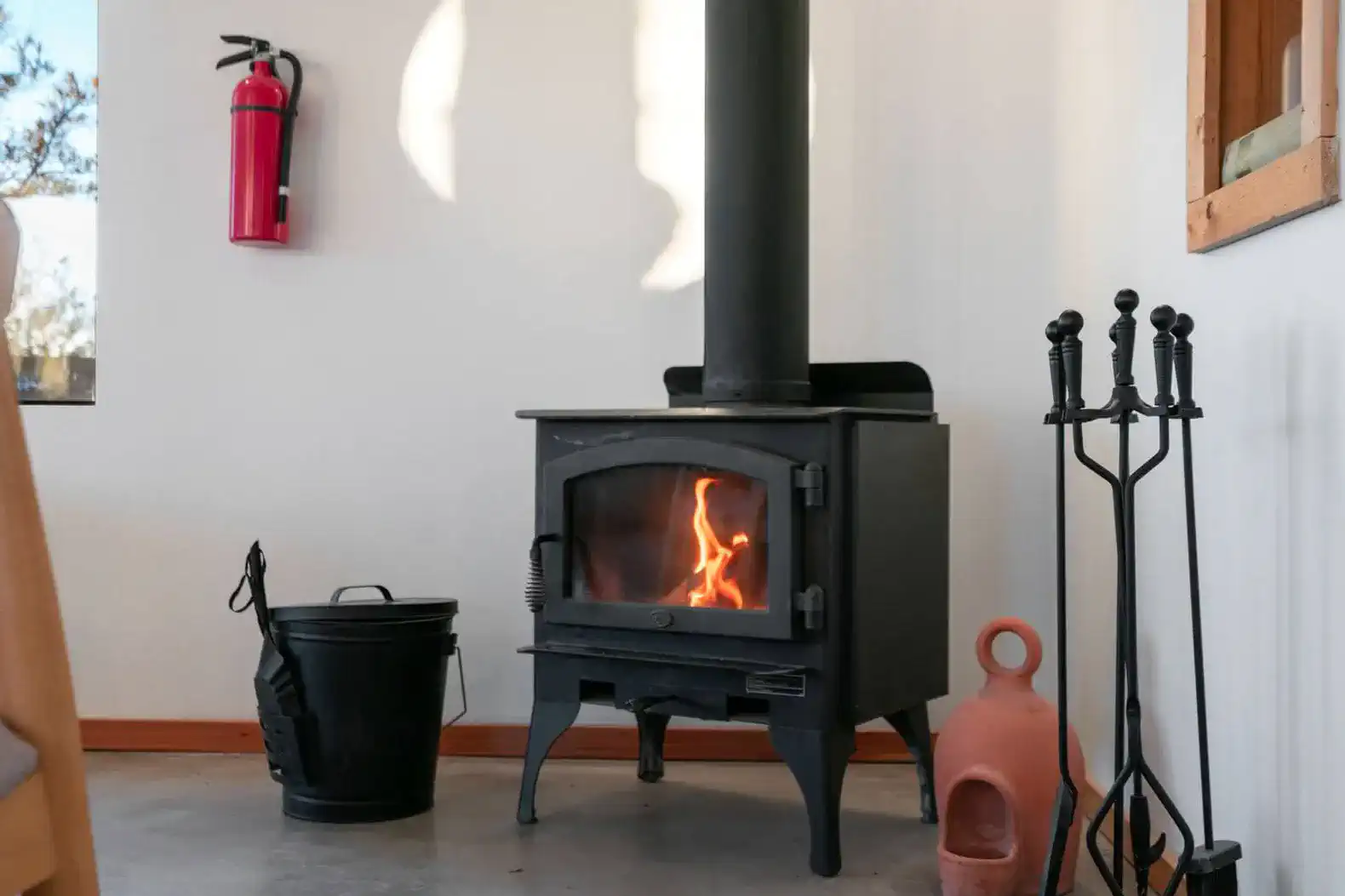 Cozy wood stove with flames, firewood tools, and a fire extinguisher nearby