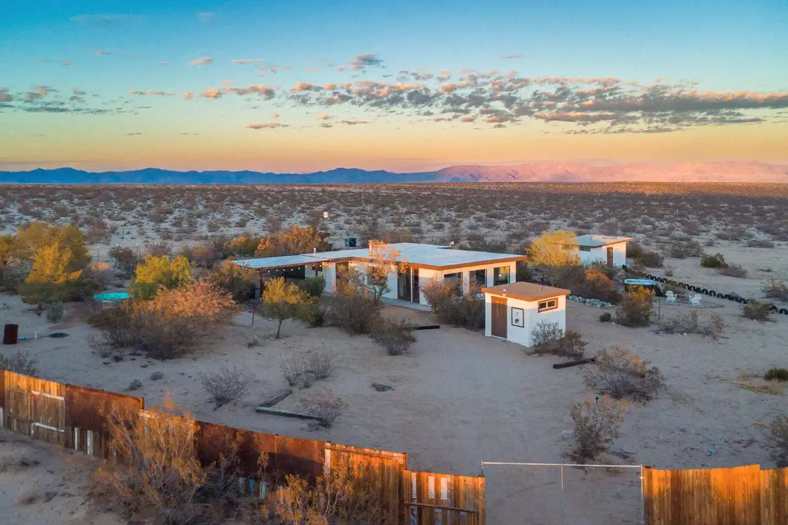 Desert landscape with a modern home surrounded by sparse vegetation and mountains in the distance