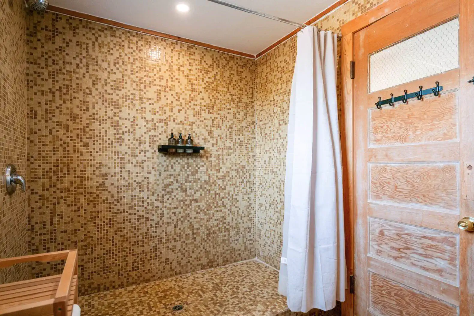 Spacious shower with mosaic tile walls and a wooden bench