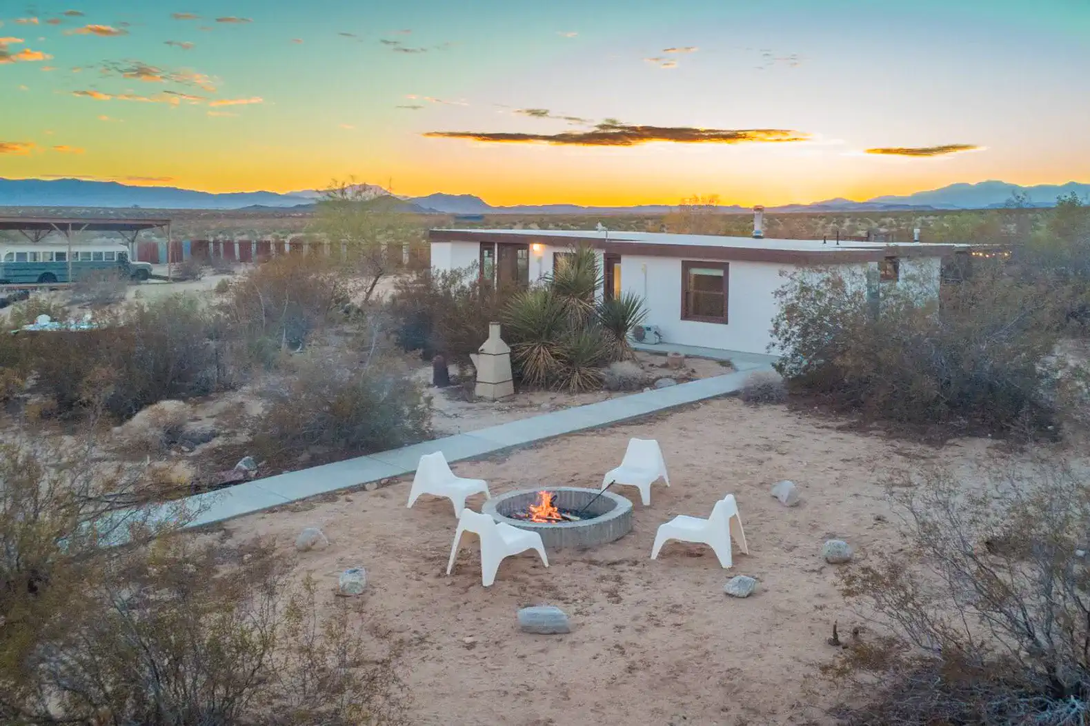 Outdoor fire pit surrounded by chairs with desert landscape and sunset in the background
