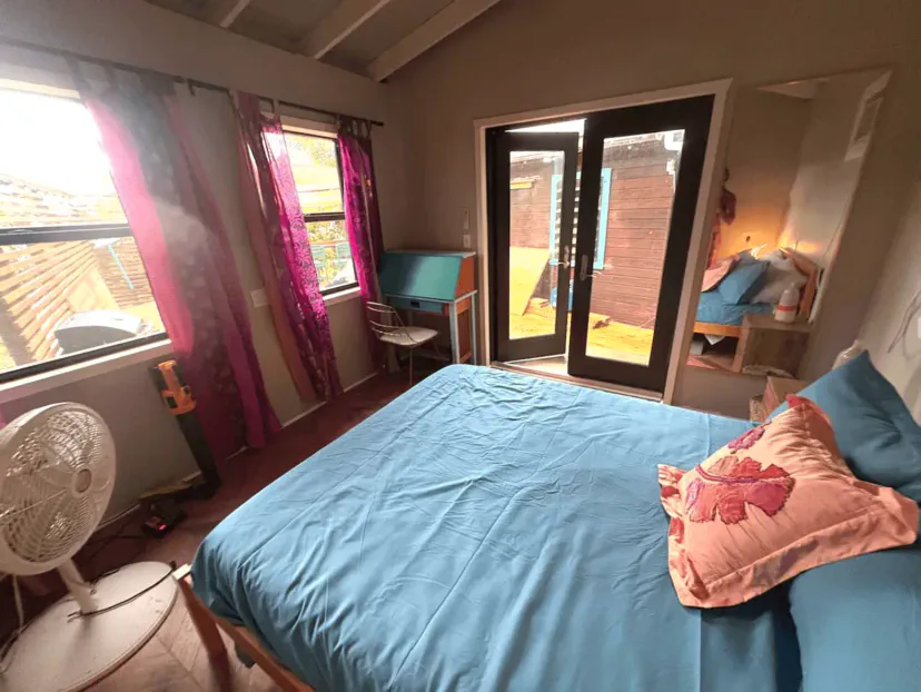 Gemütliches Schlafzimmer mit blauen Bettwaren, bunten Vorhängen und Zugang zu einem Außenbereich