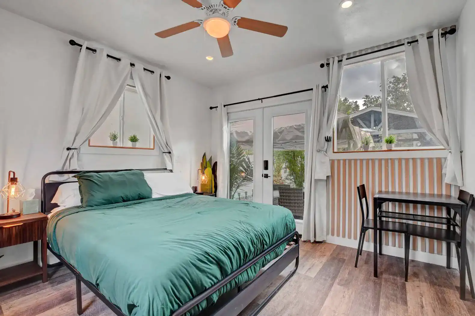 Cozy bedroom with a green bedspread, large windows, and a small dining table