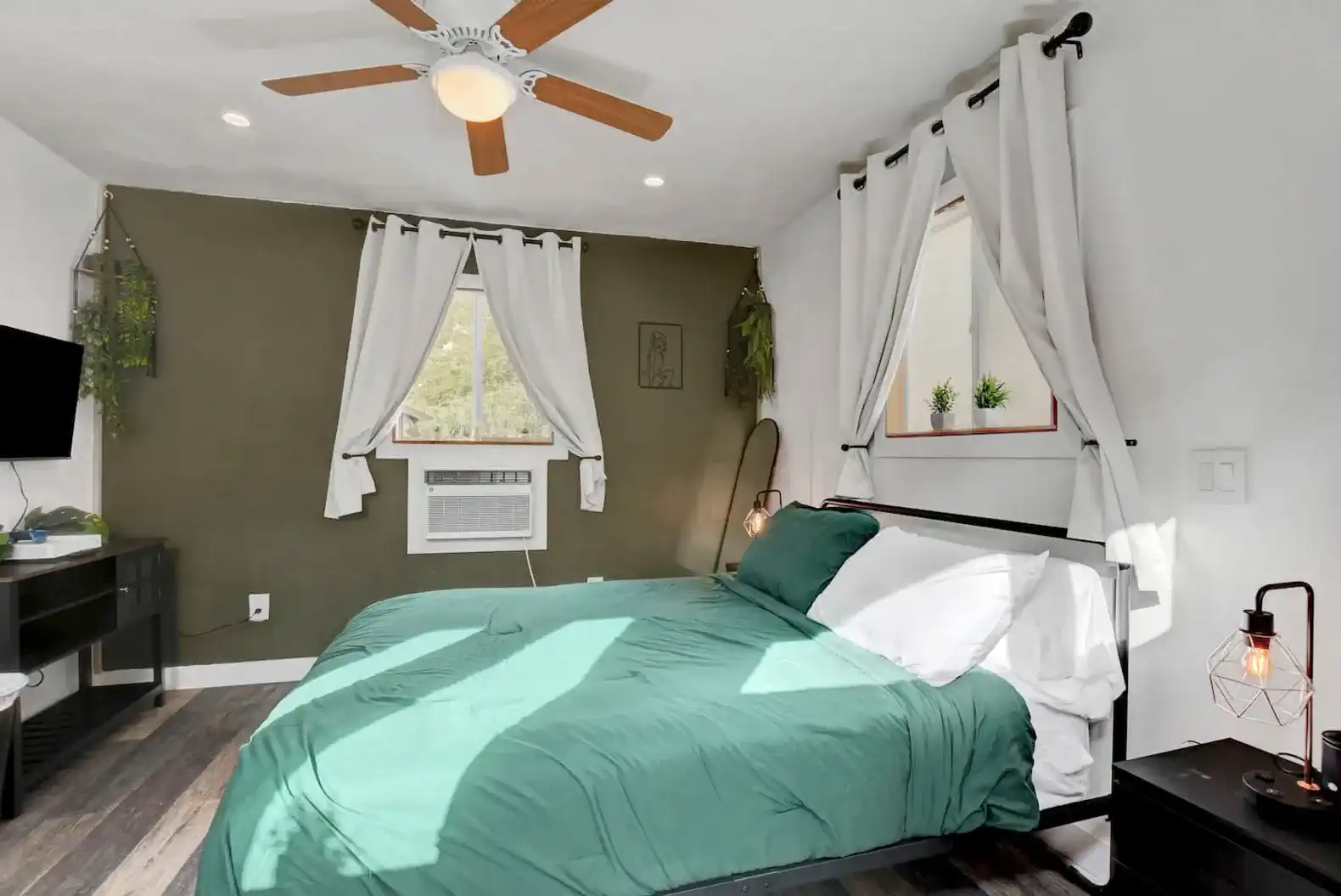 Cozy master bedroom with green bedding, ceiling fan, and natural light