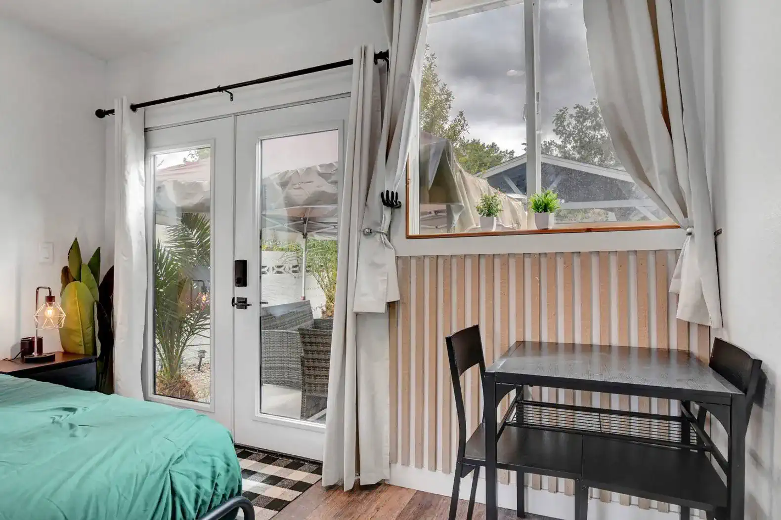 Cozy room with a bed, small table, and large window overlooking the backyard