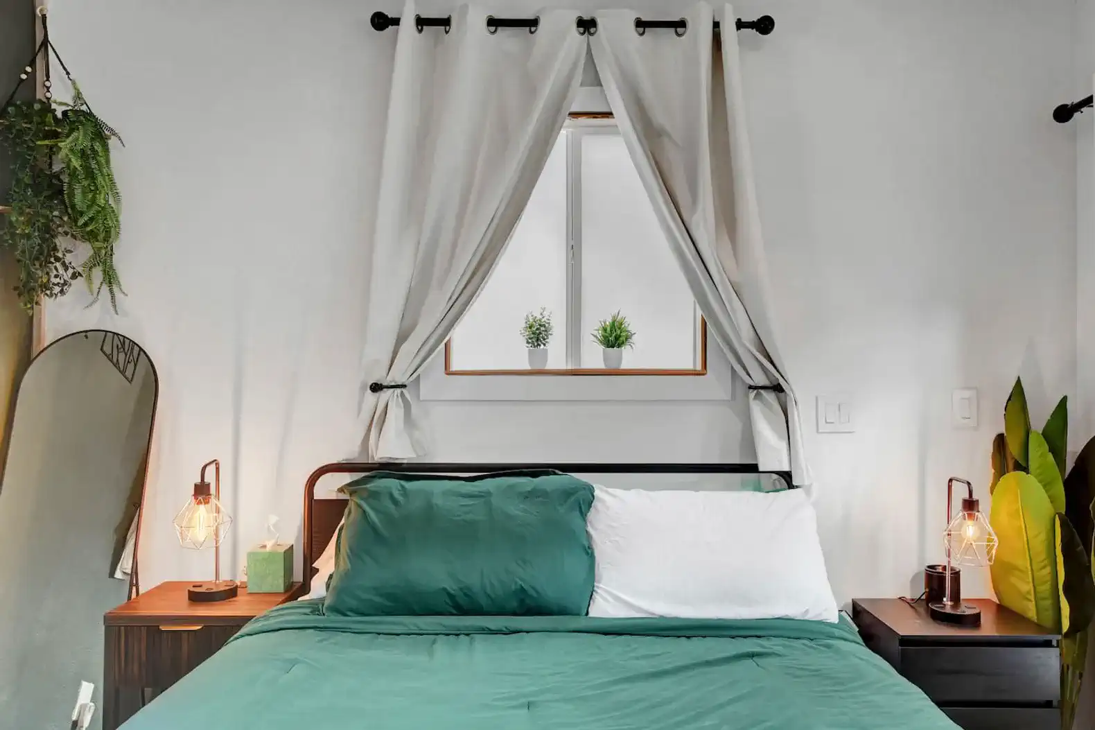 Cozy bedroom with green bedding, decorative plants by the window, and stylish lamps