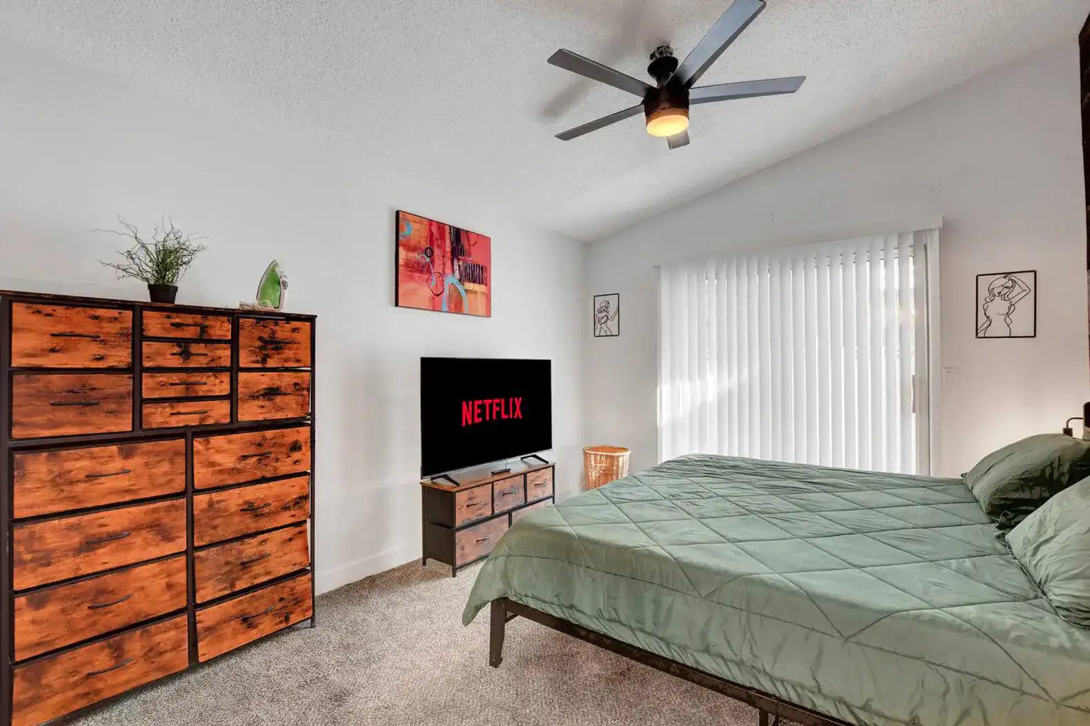 Cozy bedroom with a green quilt, dresser, and TV displaying Netflix