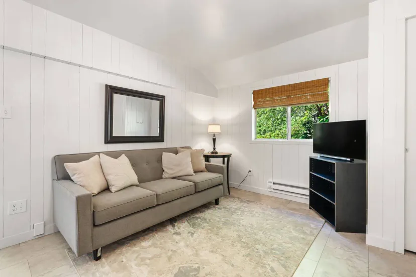 Cozy living area with a gray sofa, natural light from a window, and a TV stand against the wall