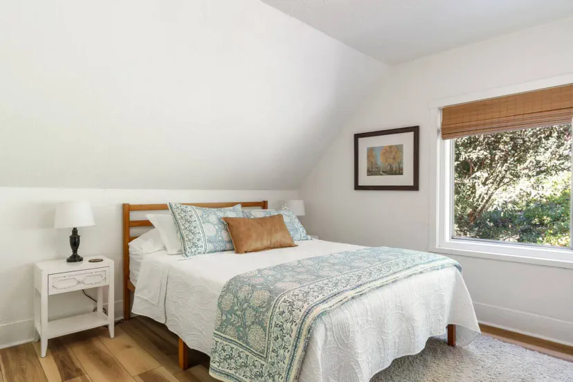 Cozy bedroom with a queen bed, soft linens, and natural light from a window overlooking greenery