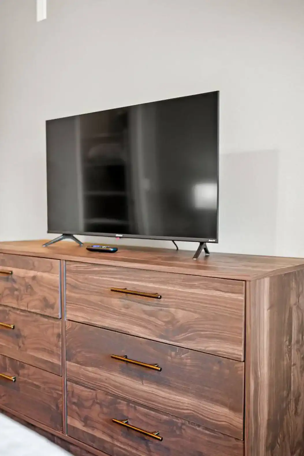 Wooden dresser with a flat-screen TV on top and remote control