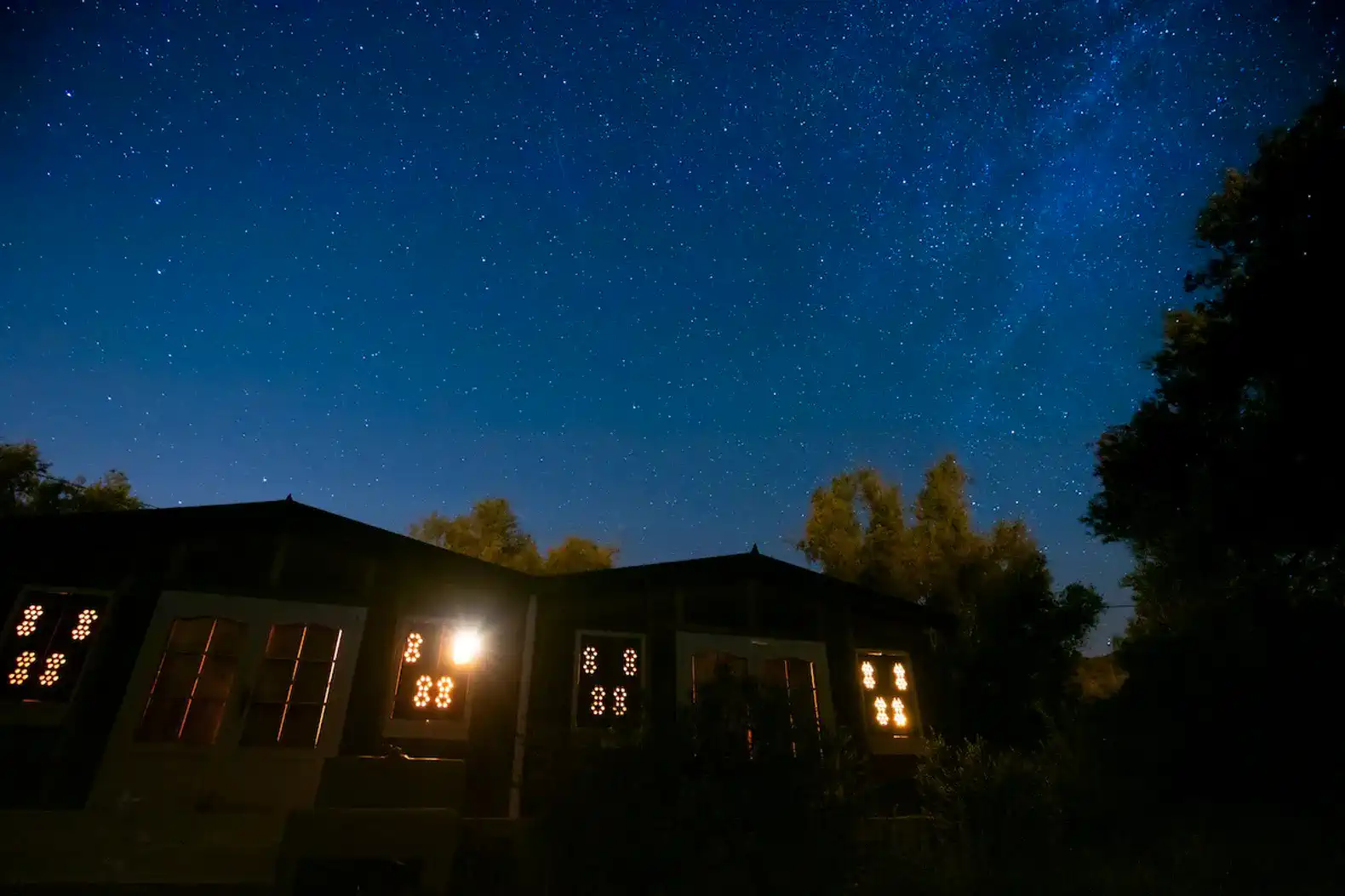 Starry night sky above a cozy cabin with illuminated windows